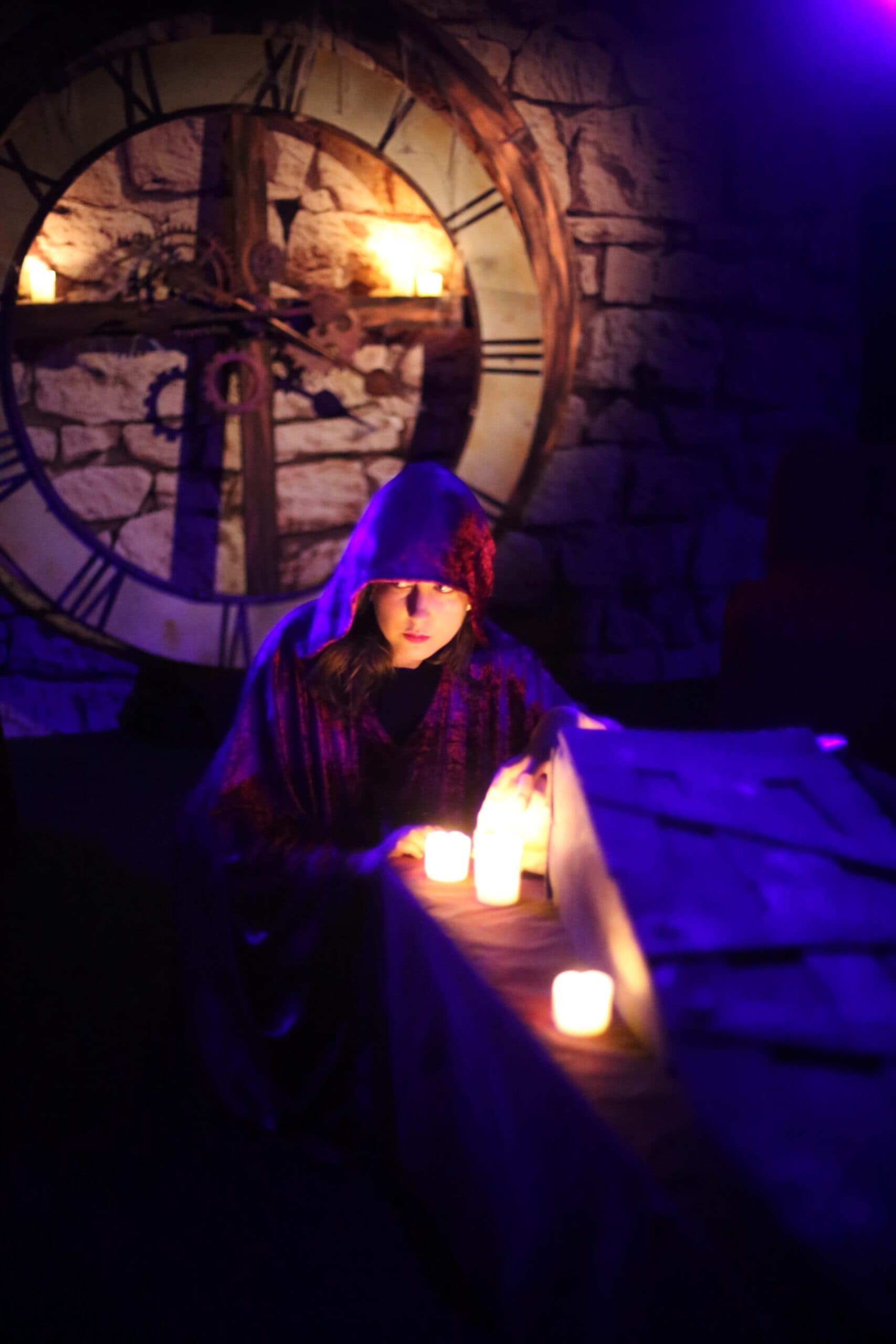 Person in a cloak in a dark, candlelit atmosphere in front of a wall clock